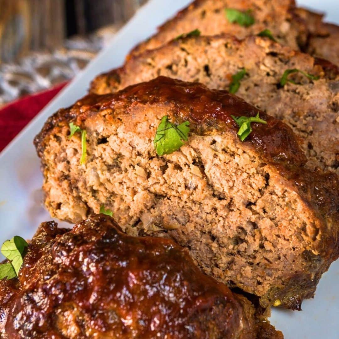 Skillet-seared slices of glazed homemade meatloaf on a white platter, topped with fresh parsley.